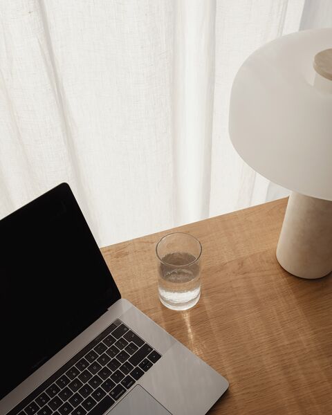 A laptop, a glass of water and a table lamp on a wooden desk